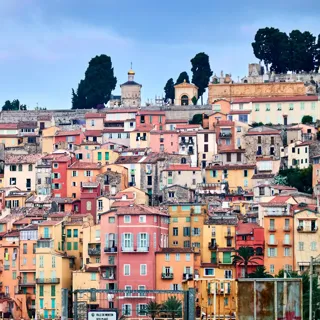 Colourful hillside town with tightly packed pastel buildings, shuttered windows and tiled roofs beneath a blue sky.