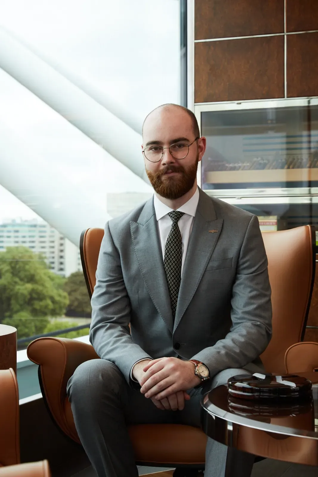 A man sat down on a leather chair wearing glasses and London views in the background
