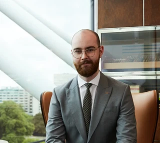 A man sat down on a leather chair wearing glasses and London views in the background