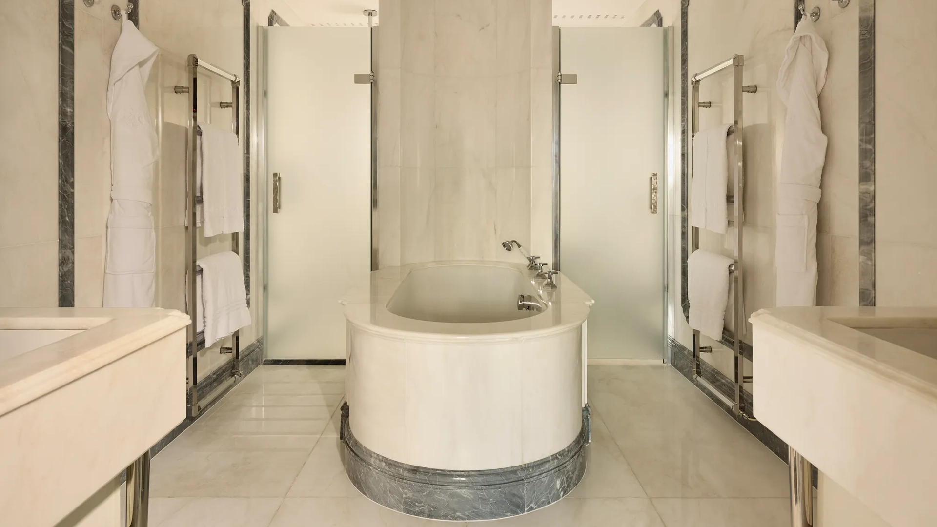 Luxurious marble bathroom with central oval bathtub, frosted glass doors, and towel rails.