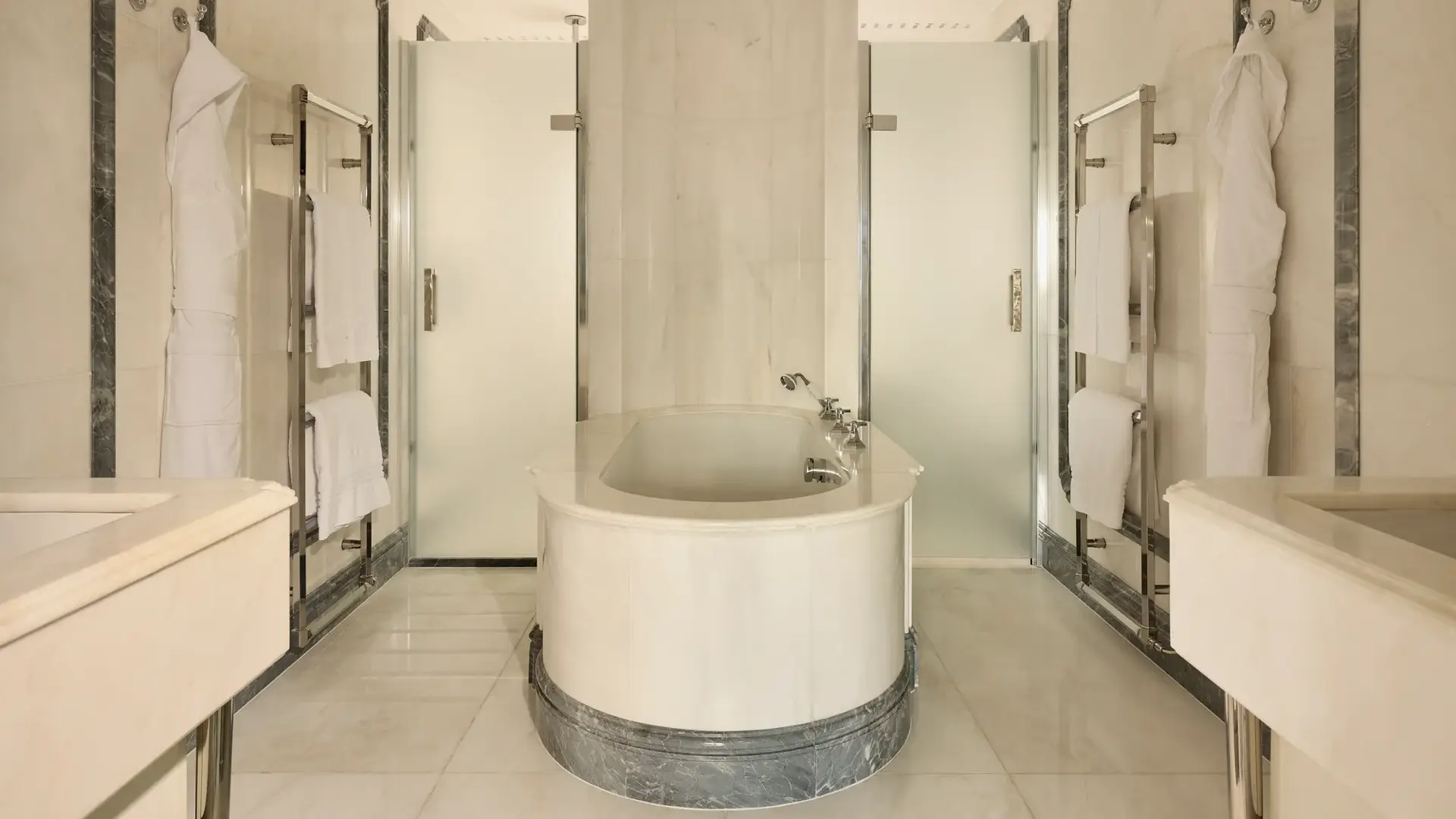 Luxurious marble bathroom with central oval bathtub, frosted glass doors, and towel rails.
