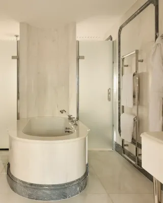 Luxurious marble bathroom with central oval bathtub, frosted glass doors, and towel rails.