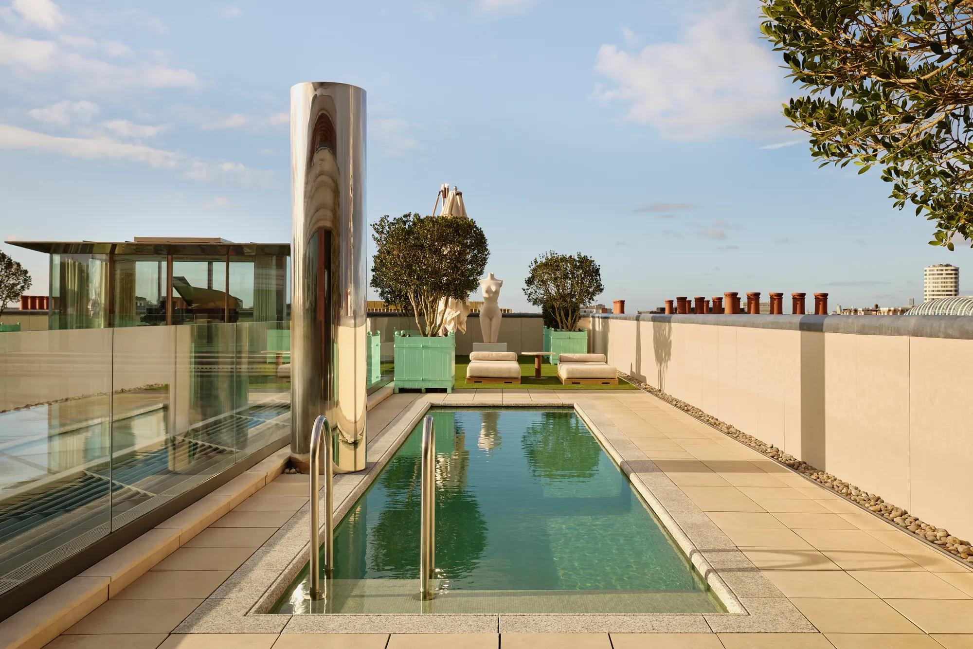 Rooftop terrace at Claridge’s with a narrow swimming pool, sun loungers, and city skyline views under a clear sky.