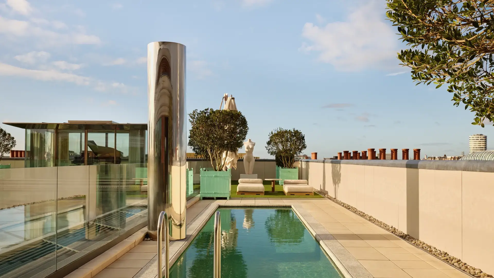 Rooftop terrace at Claridge’s with a narrow swimming pool, sun loungers, and city skyline views under a clear sky.