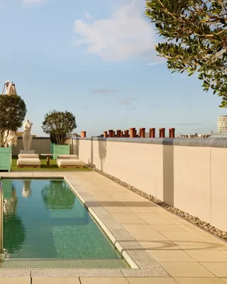 Rooftop terrace at Claridge’s with a narrow swimming pool, sun loungers, and city skyline views under a clear sky.