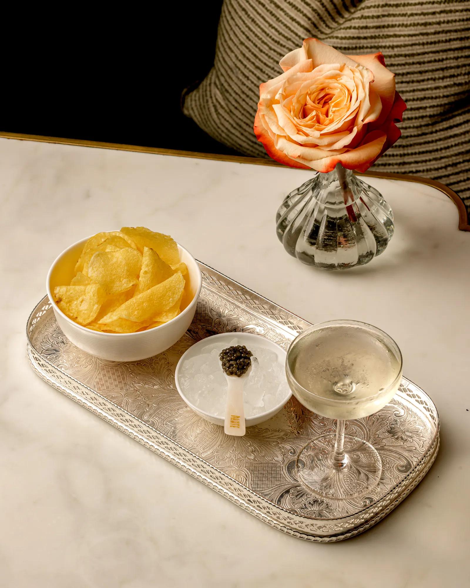 A coupe glass served with caviar, crisps and a rose on a silver tray.