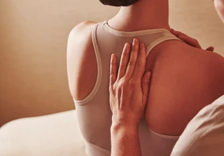 Therapist placing hands on a person's upper back during a seated spa treatment, with the person wearing a sports bra.