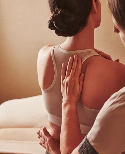 Therapist placing hands on a person's upper back during a seated spa treatment, with the person wearing a sports bra.
