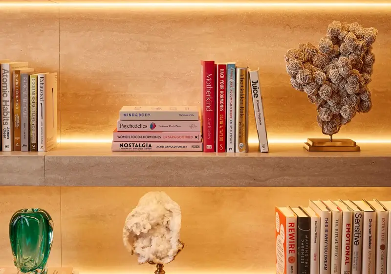 Illuminated stone shelves displaying books, decorative glass bottles and sculptural objects.