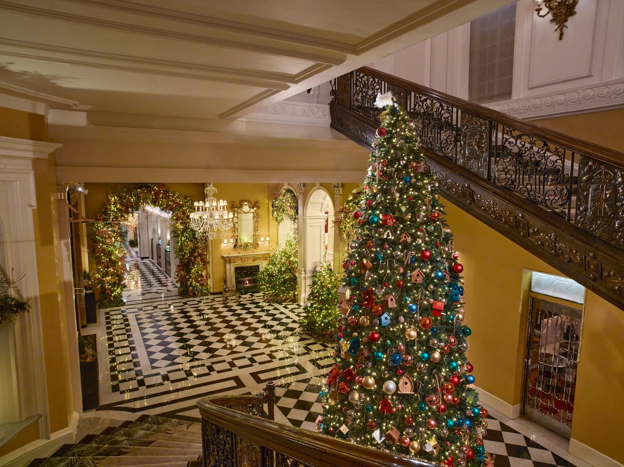Grand lobby with black and white marble floor, sweeping staircase, and large decorated Christmas tree with festive garlands and lights.
