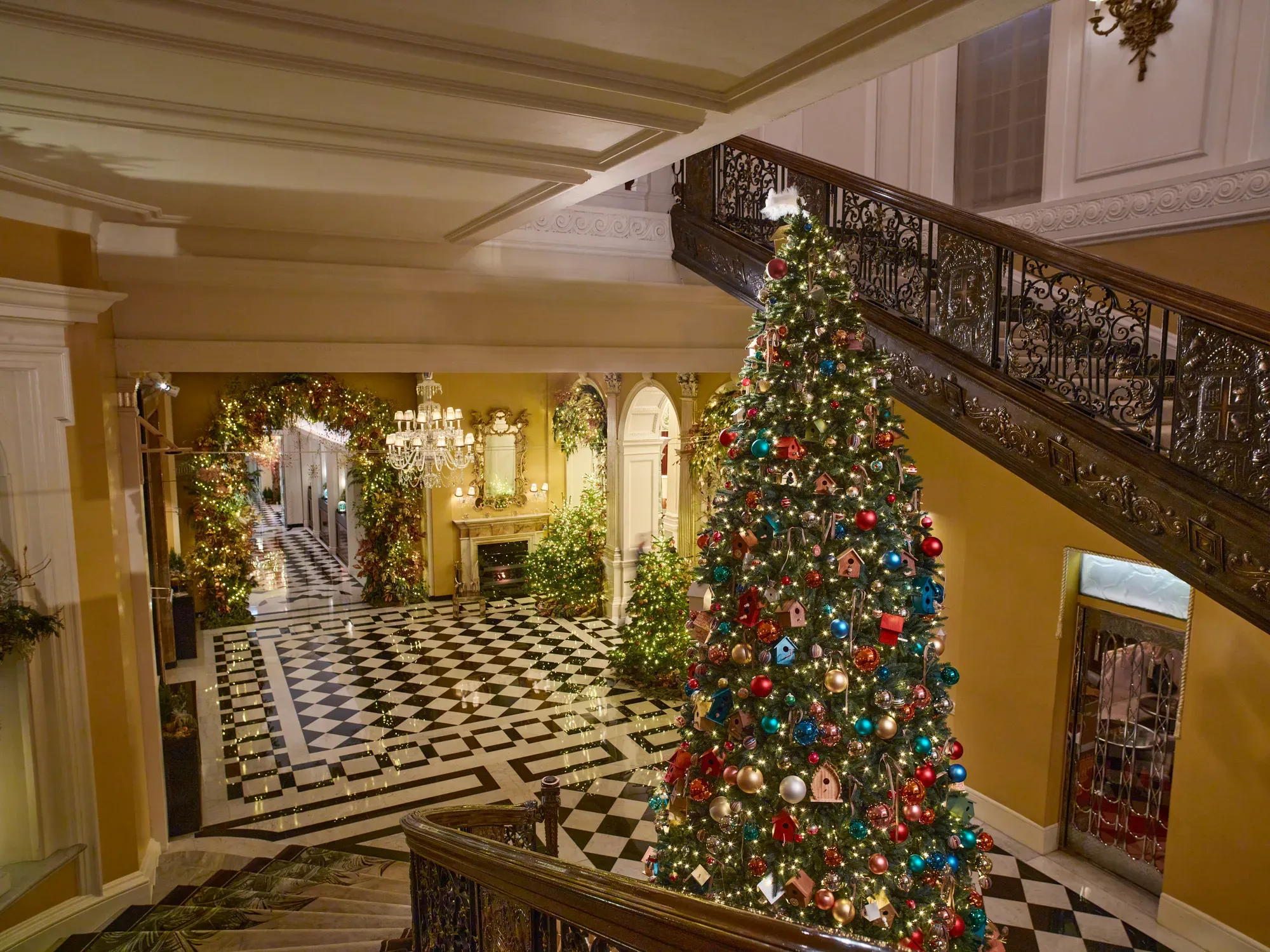 Grand lobby with black and white marble floor, sweeping staircase, and large decorated Christmas tree with festive garlands and lights.