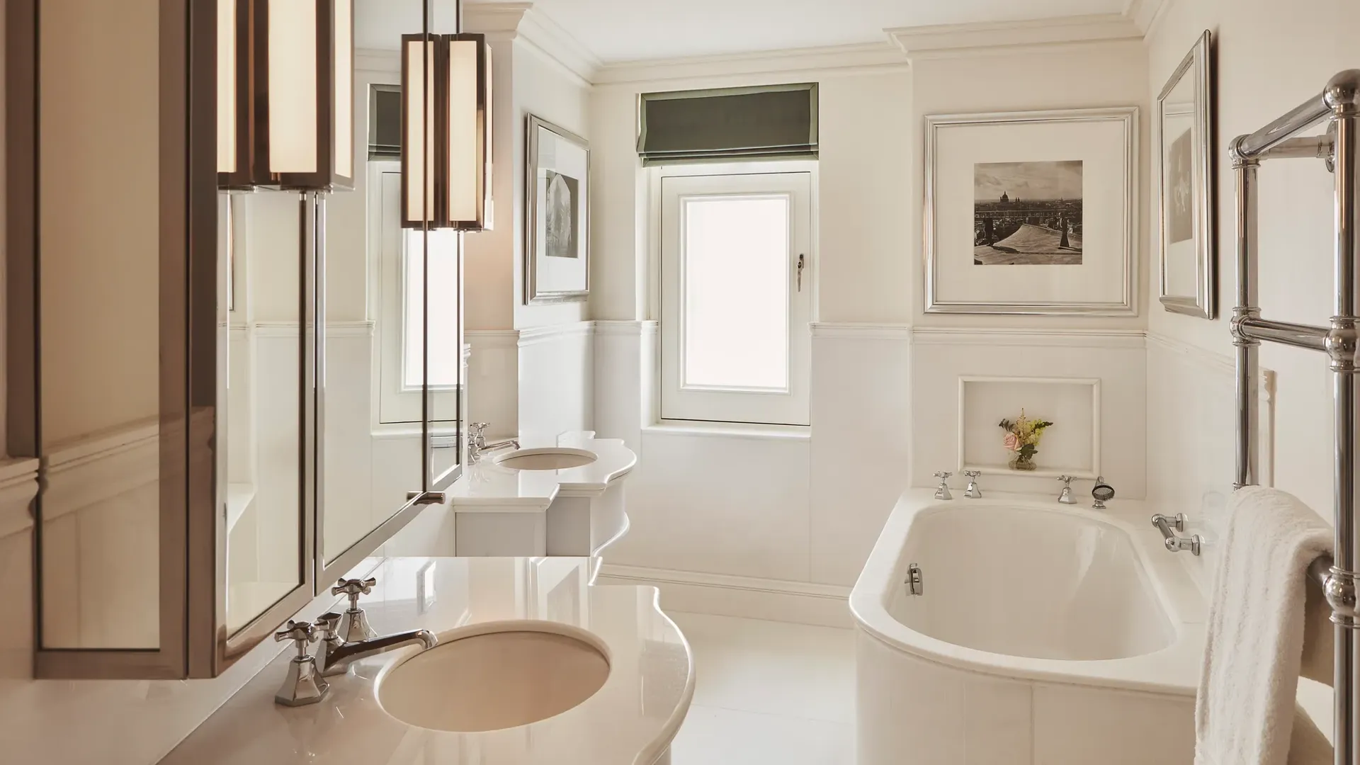 Bright bathroom with freestanding bathtub, double sinks, framed artwork, and a small window above.