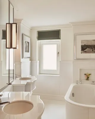 Bright bathroom with freestanding bathtub, double sinks, framed artwork, and a small window above.