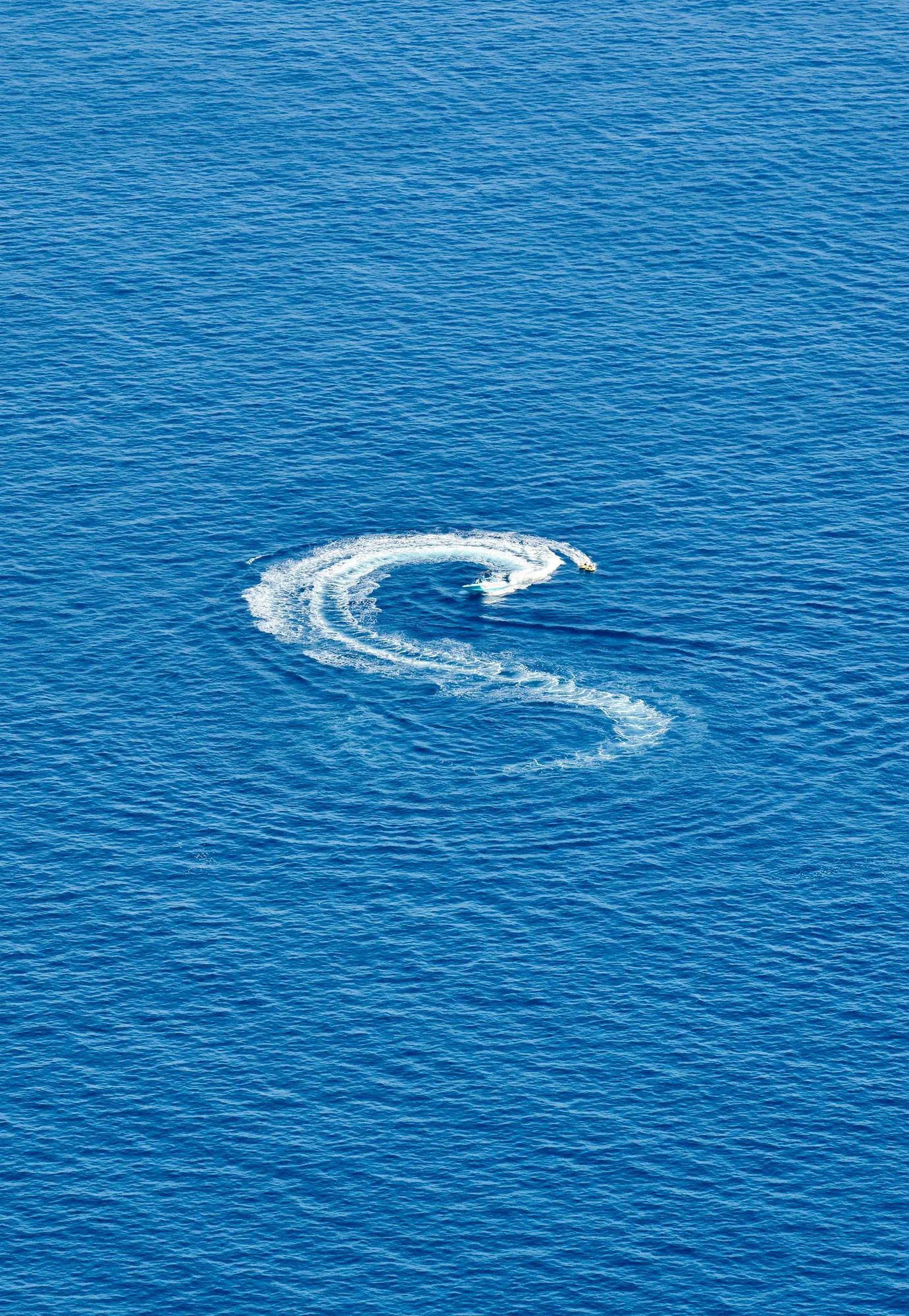 A speedboat creates an S-shaped trail of white foam across the deep blue sea.