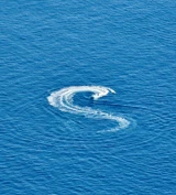 A speedboat creates an S-shaped trail of white foam across the deep blue sea.