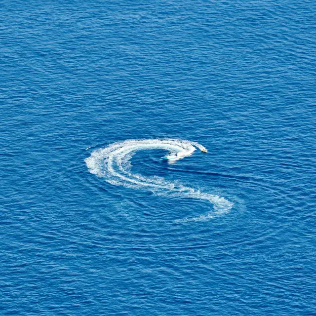A speedboat creates an S-shaped trail of white foam across the deep blue sea.