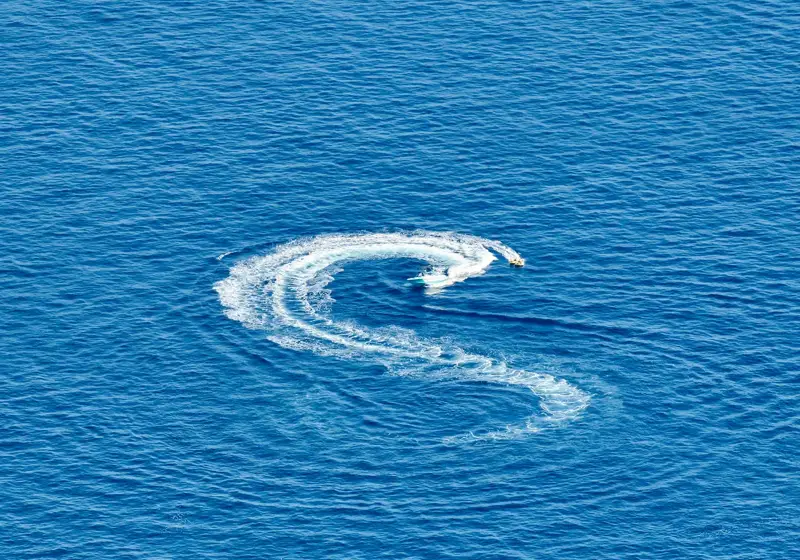 A speedboat creates an S-shaped trail of white foam across the deep blue sea.