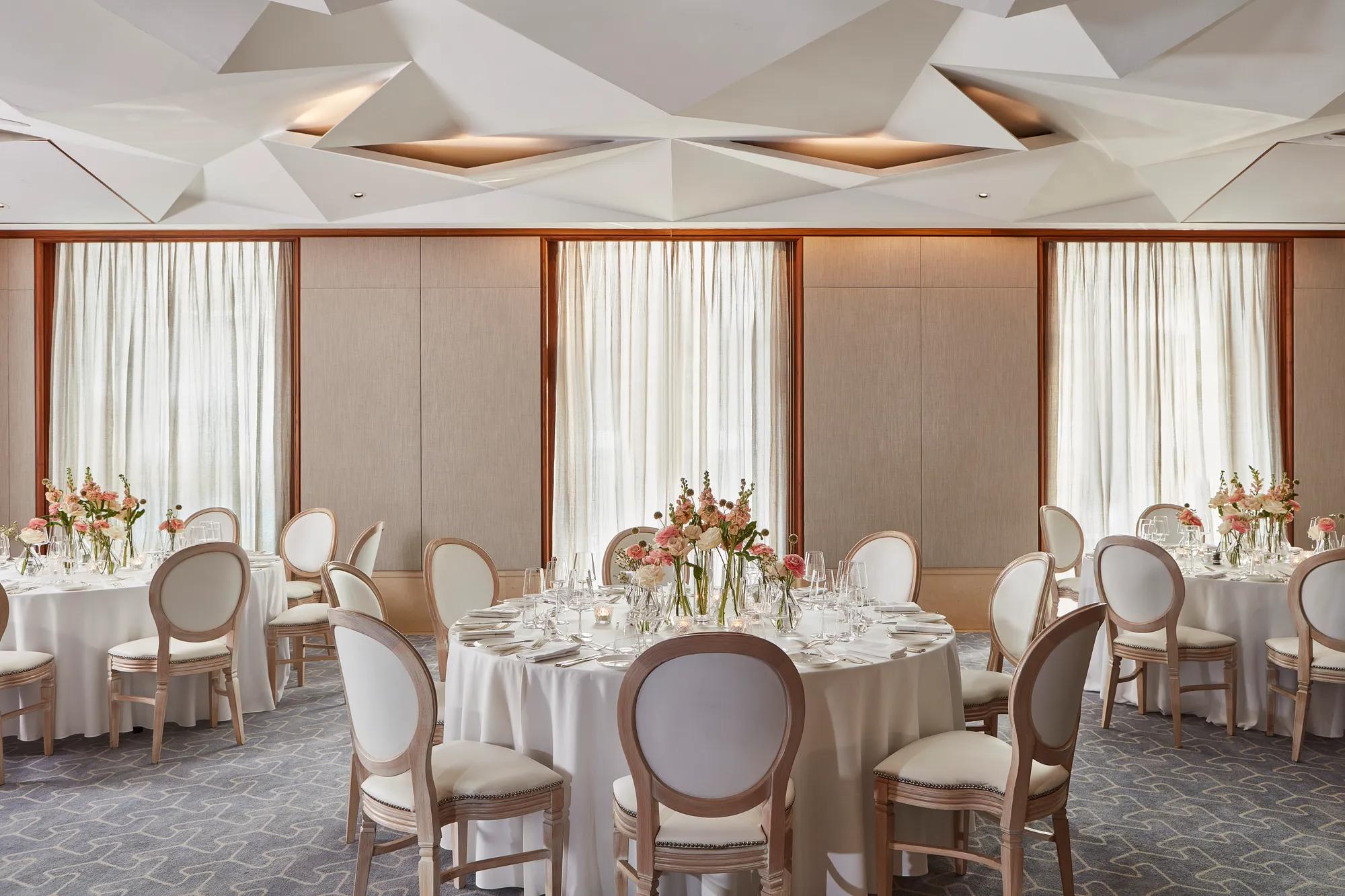 Round tables with white linens and pastel flower arrangements under geometric ceiling lights.
