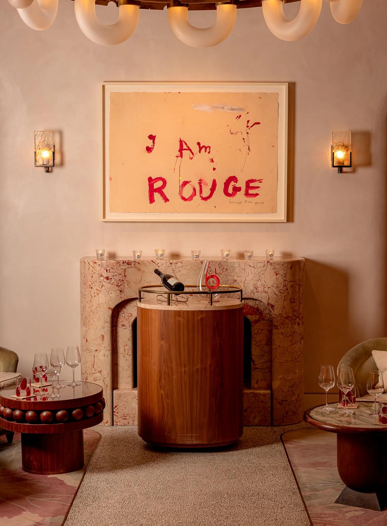 A dimly lit cocktail bar with deep red walls, plush velvet seating, a sculptural red bar counter, and soft spotlighting that highlights bottles and glassware, creating an intimate, luxurious atmosphere