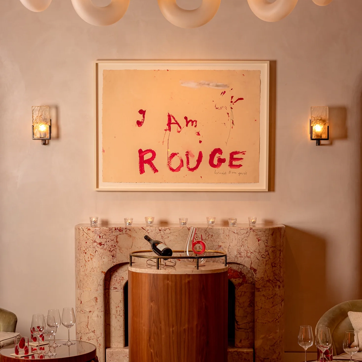 A dimly lit cocktail bar with deep red walls, plush velvet seating, a sculptural red bar counter, and soft spotlighting that highlights bottles and glassware, creating an intimate, luxurious atmosphere