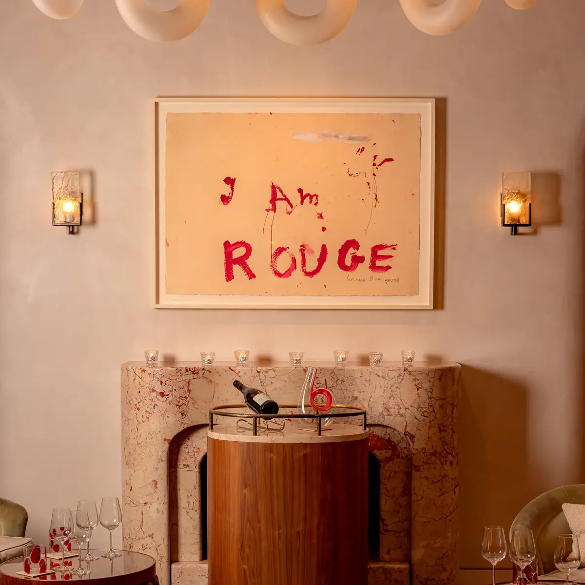 A dimly lit cocktail bar with deep red walls, plush velvet seating, a sculptural red bar counter, and soft spotlighting that highlights bottles and glassware, creating an intimate, luxurious atmosphere