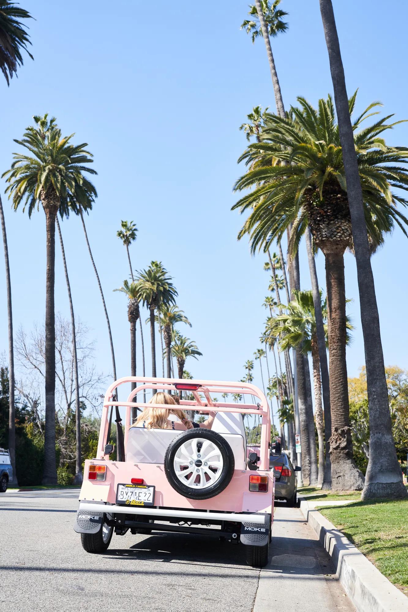Pink Moke car driving through palm tree lined street in Bevely Hills.