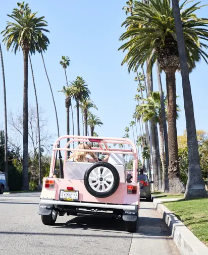 Pink Moke car driving through palm tree lined street in Bevely Hills.