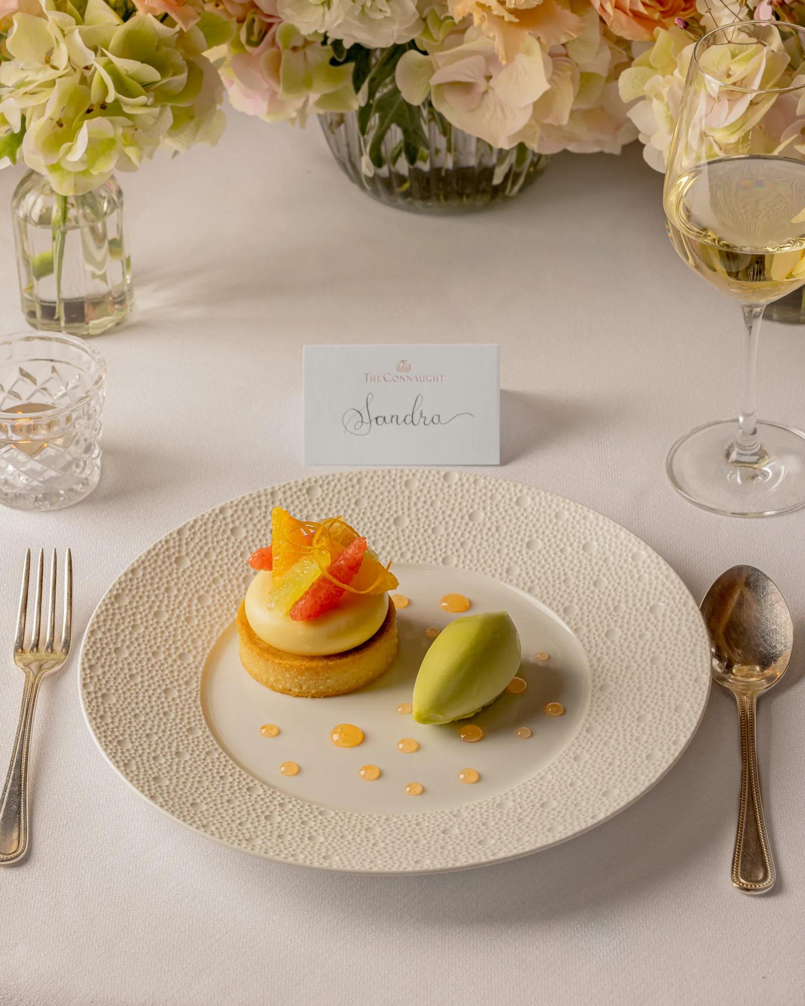 Plated citrus dessert with a scoop of sorbet at an elegant place setting, with a name card and floral centrepieces.