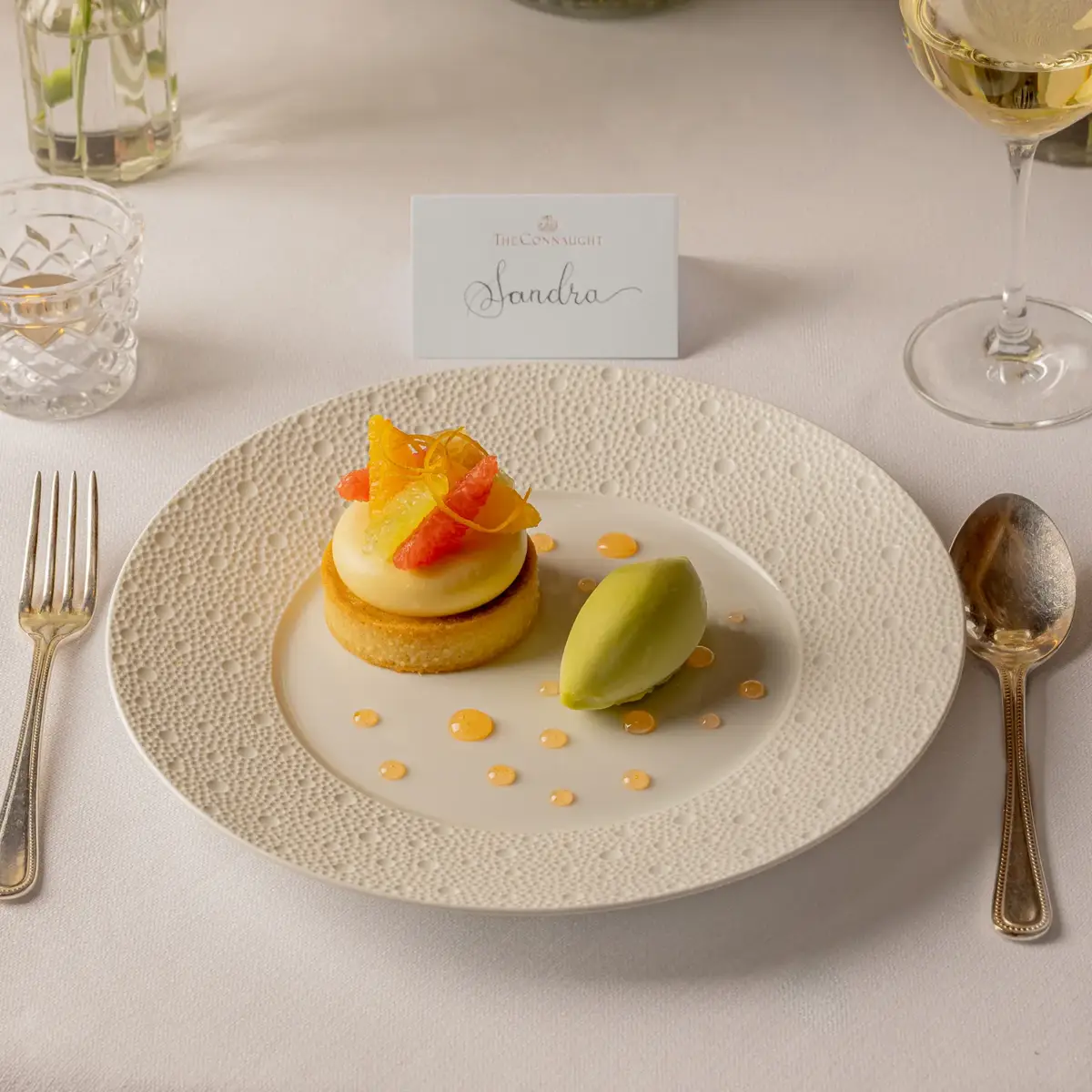 Plated citrus dessert with a scoop of sorbet at an elegant place setting, with a name card and floral centrepieces.
