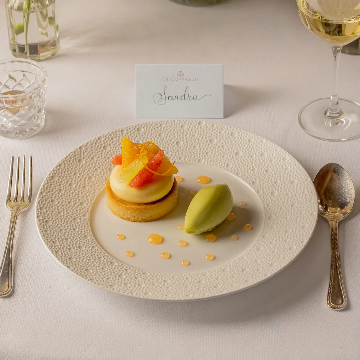 Plated citrus dessert with a scoop of sorbet at an elegant place setting, with a name card and floral centrepieces.
