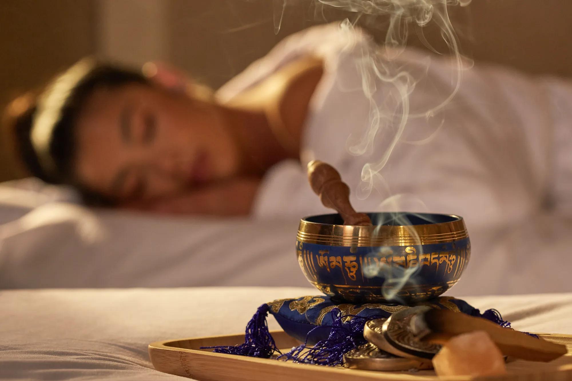 Aromatic incense bowl emitting smoke beside a female guest resting during spa treatment