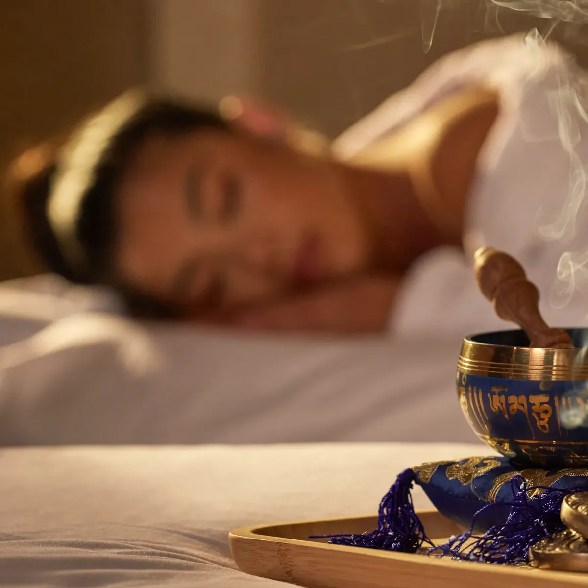 Aromatic incense bowl emitting smoke beside a female guest resting during spa treatment