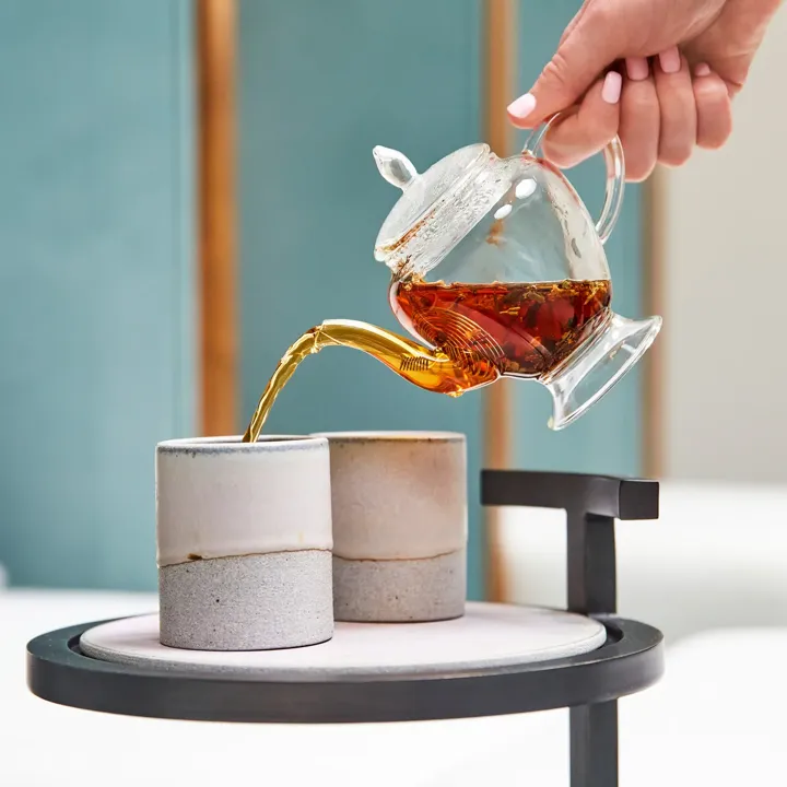 Tea being poured into ceramic cups on side table in spa relaxation area