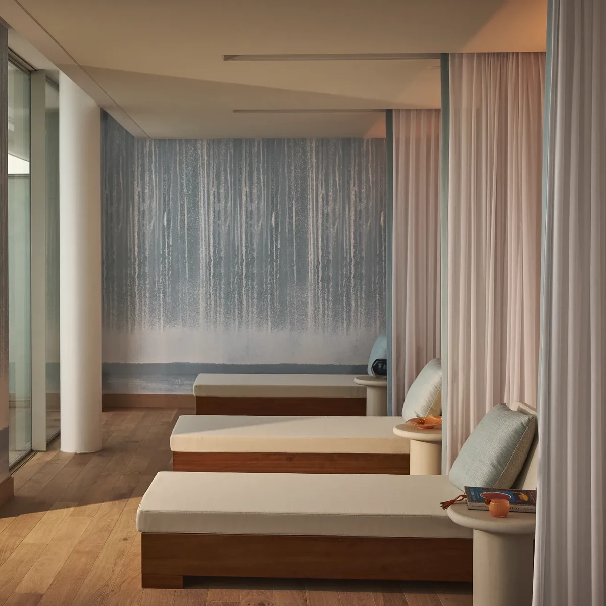 Relaxation area in Surrenne featuring white lounge chairs with soft cushions, separated by light curtains, and a calming wall with a gradient blue design, evoking a peaceful and serene atmosphere.