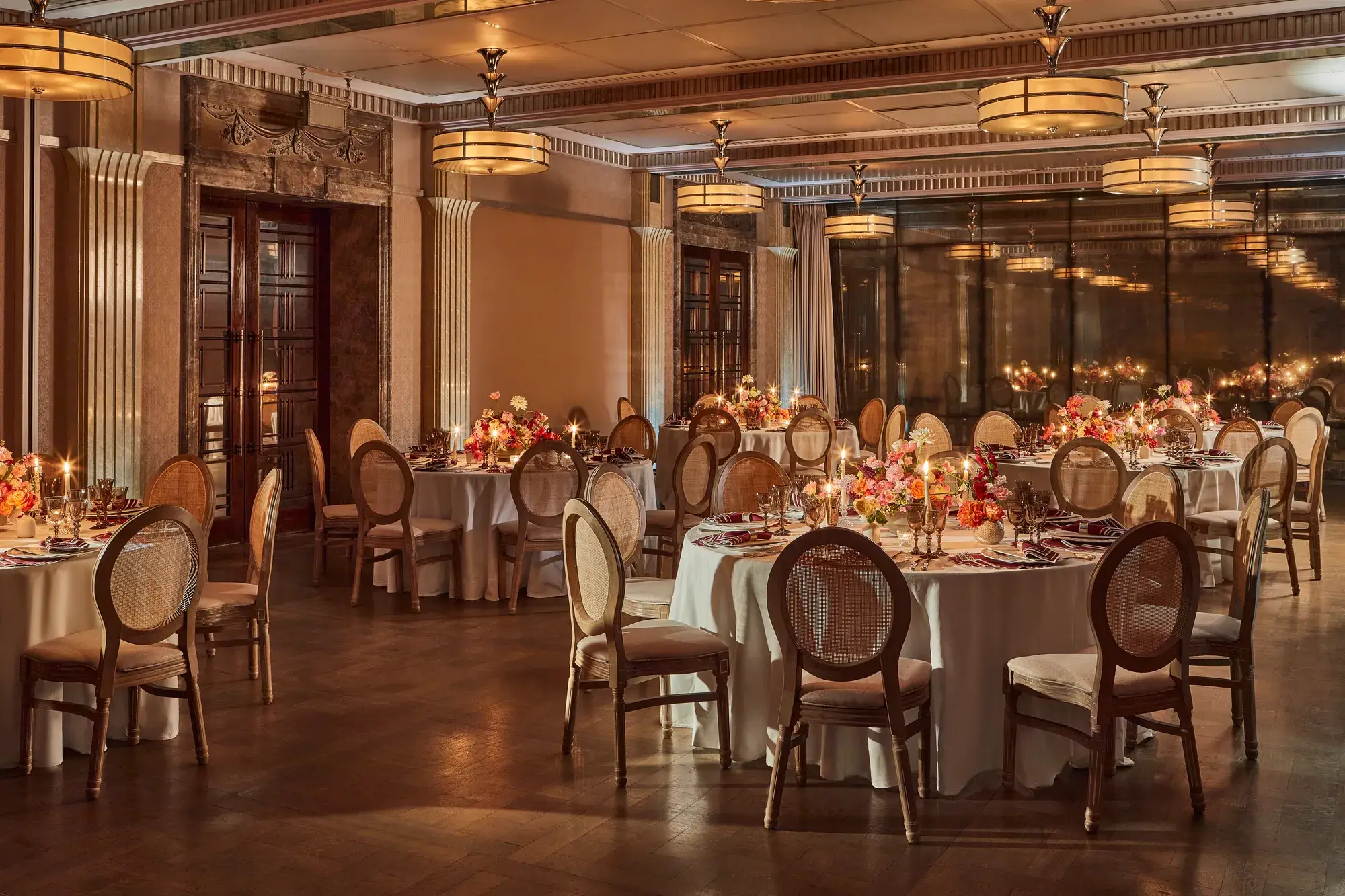 Elegant banquet room with round tables set for dinner, soft lighting, and floral centerpieces with candles.