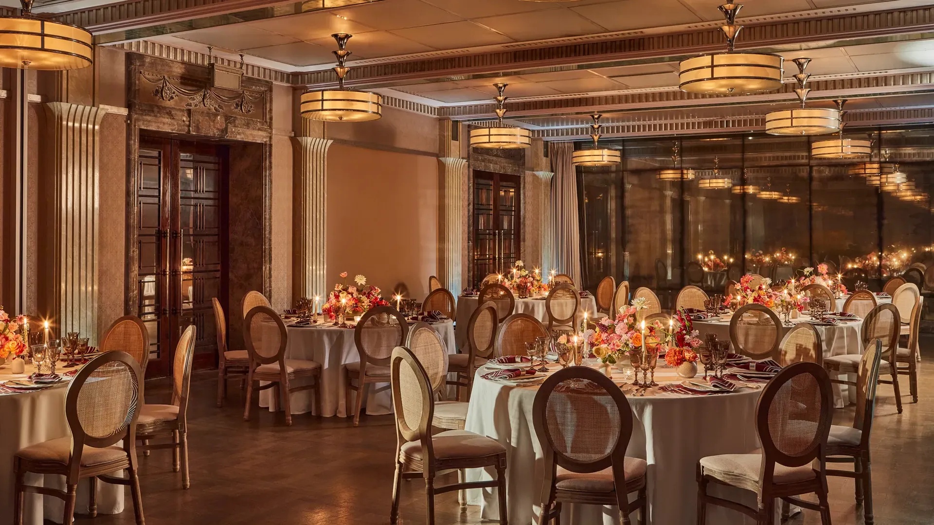 Elegant banquet room with round tables set for dinner, soft lighting, and floral centerpieces with candles.