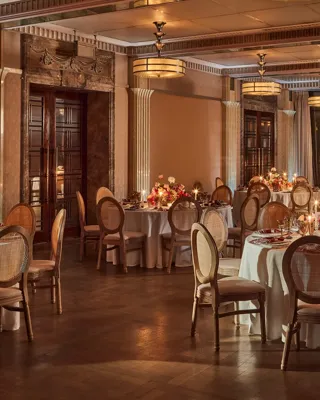 Elegant banquet room with round tables set for dinner, soft lighting, and floral centerpieces with candles.