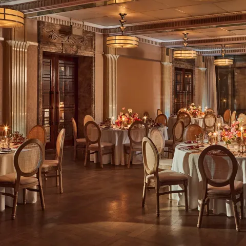 Elegant banquet room with round tables set for dinner, soft lighting, and floral centerpieces with candles.