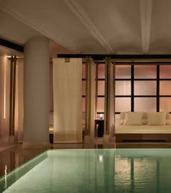 Tranquil indoor pool at The Maybourne Riviera with a softly lit daybed framed by sheer curtains and columns, creating an elegant and serene spa atmosphere.