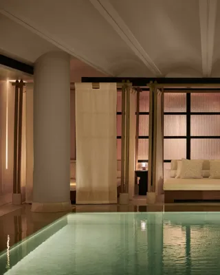 Tranquil indoor pool at The Maybourne Riviera with a softly lit daybed framed by sheer curtains and columns, creating an elegant and serene spa atmosphere.