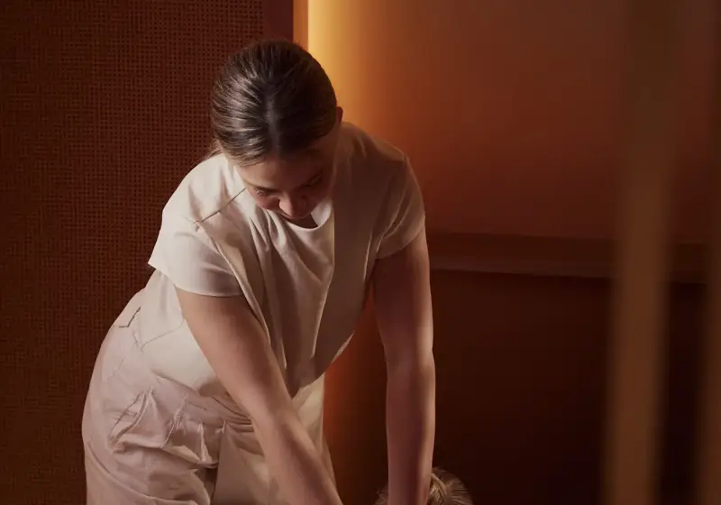 Spa therapist performing deep tissue massage on guest lying face down on treatment bed.