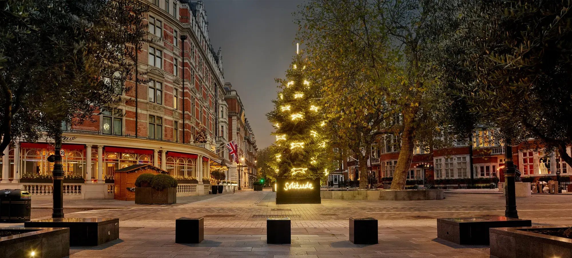 Golden-lit Christmas tree with “Solitude” sign outside grand London hotel at dusk.