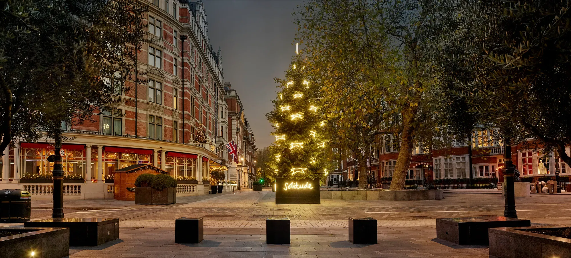 Golden-lit Christmas tree with “Solitude” sign outside grand London hotel at dusk.