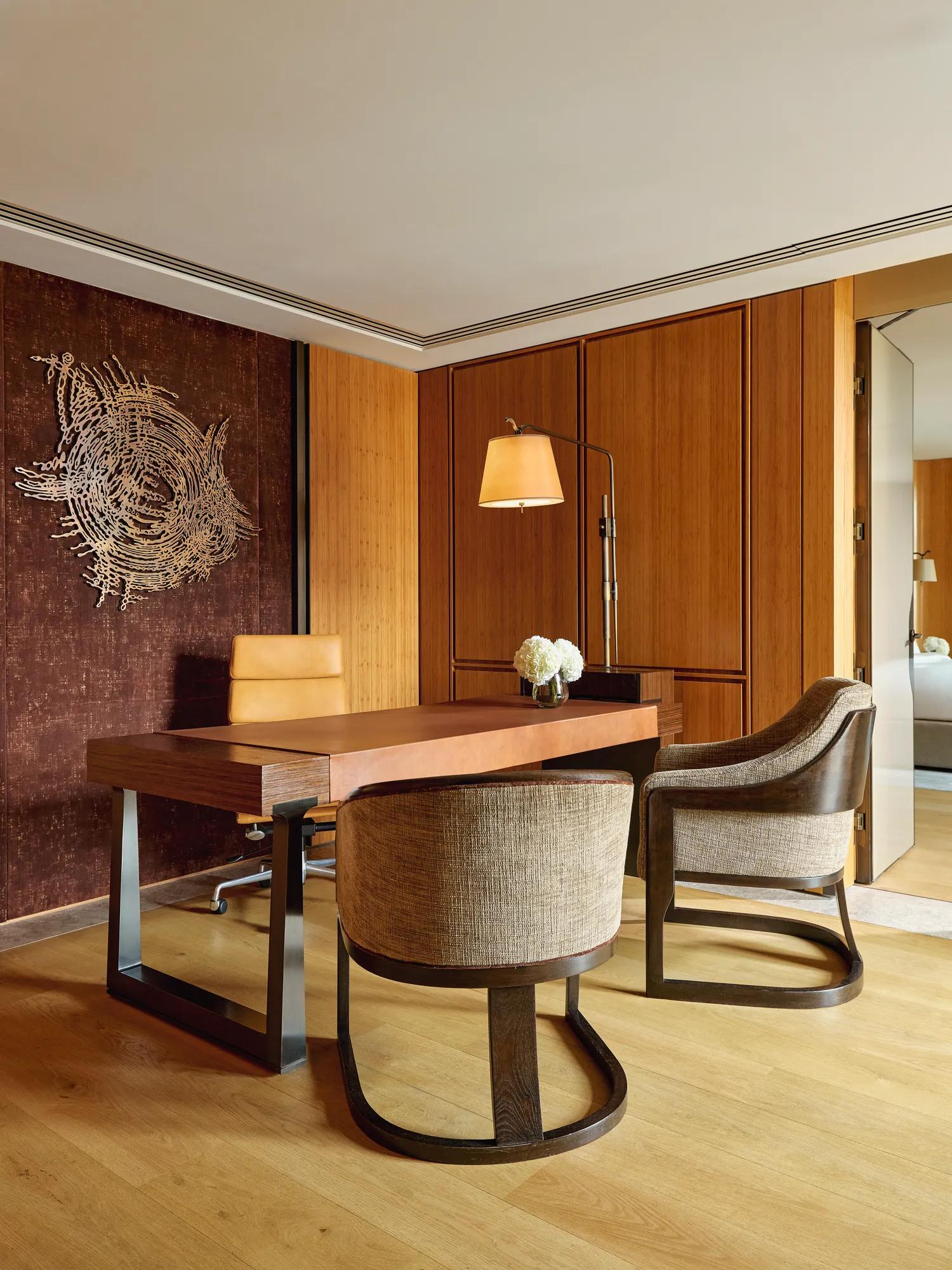 Elegant study with wooden desk, modern chairs, wall sculpture, and warm lighting in the Opus Suite