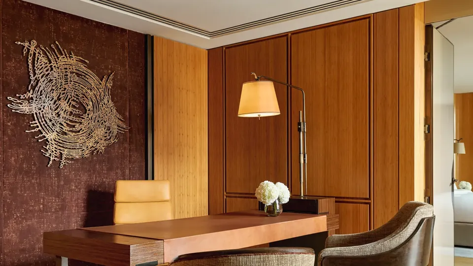 Elegant study with wooden desk, modern chairs, wall sculpture, and warm lighting in the Opus Suite