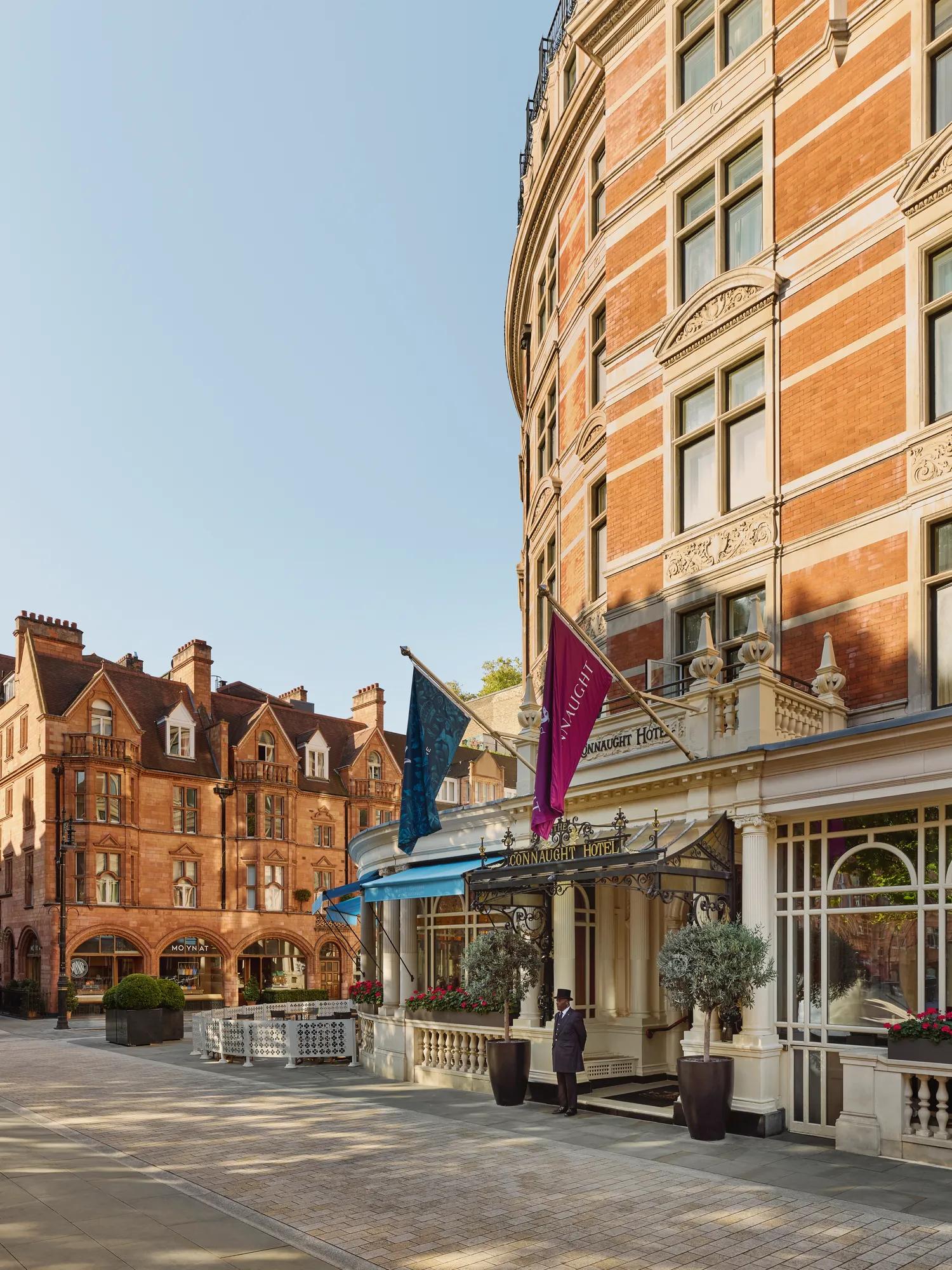 Red-brick hotel façade with flags and canopy entrance, overlooking a quiet paved courtyard with surrounding historic buildings