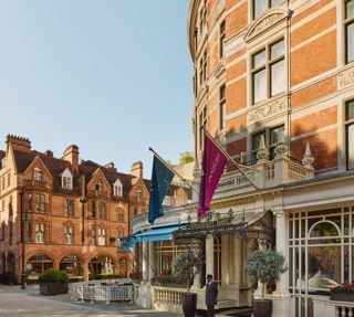 Red-brick hotel façade with flags and canopy entrance, overlooking a quiet paved courtyard with surrounding historic buildings