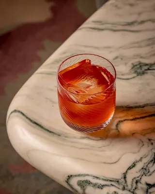 Negroni-style orange cocktail in a patterned glass resting on a marbled table edge.