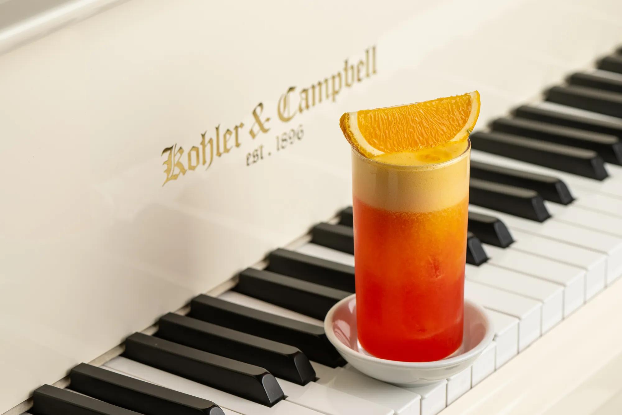 Orange-topped girabaldi cocktail placed on the keys of a white Kohler and Campbell piano.