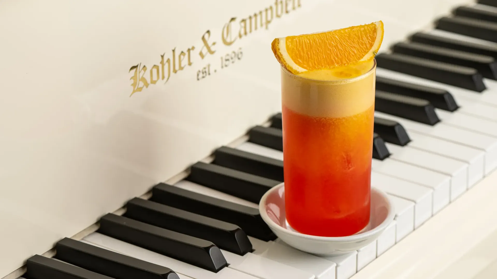 Orange-topped girabaldi cocktail placed on the keys of a white Kohler and Campbell piano.